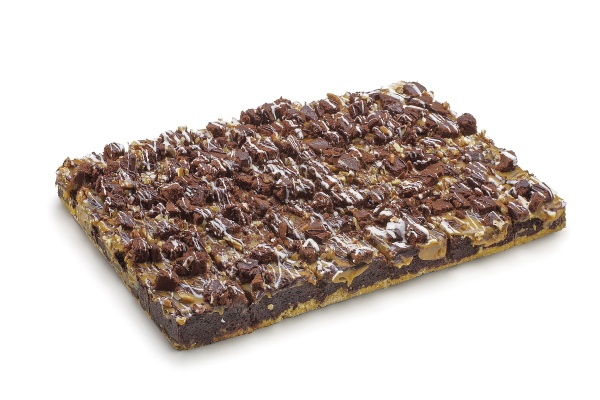 Una base de crumble, brownie en el medio y una fina capa de caramelo, daditos de bizcocho de chocolate, nueces pecan y una decoración de cobertura de choclate blanco y negro