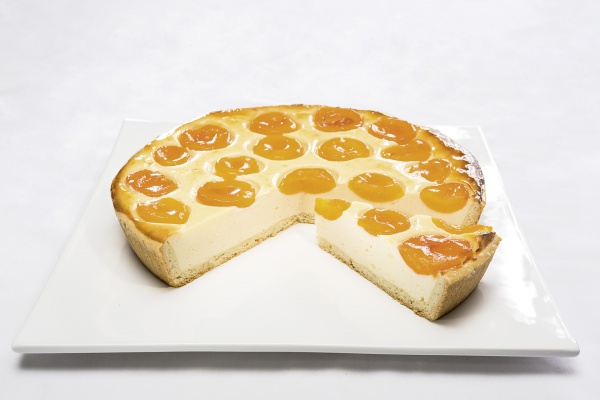 Ein Käsekuchen mit frischem Quark und Sauerrahm, reichlich bedeckt mit Aprikosenhälften und verfeinert mit Eierschneckenmasse. Der Kuchen ist mit Gelee leicht abgeglänzt.